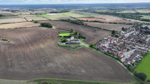 An aerial image of land that is set to be developed near Clowne. It is mostly brown fields, with homes to the right.