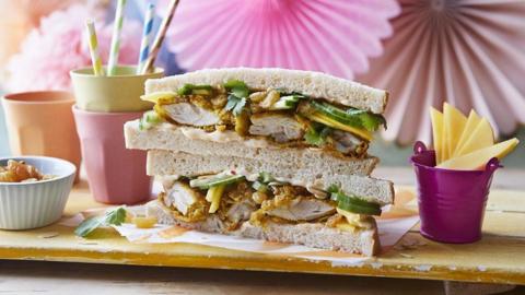 Coronation chicken sandwich on white sliced brea next to some plastic cups and straws.