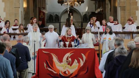 A group of female priests standing at the front of church leading a congregation in a group prayer