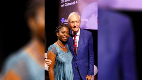 Dr Precious Lunga (left), wearing a blue dress and Jon Snow (right) wearing a blue suit.