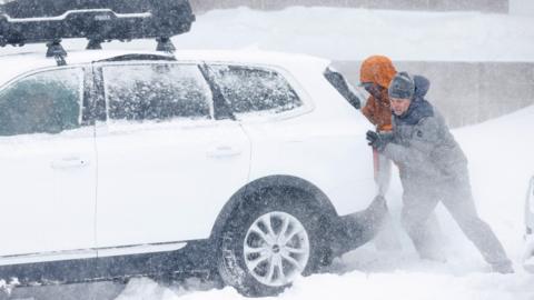 Two people pushing a car in a snowstorm