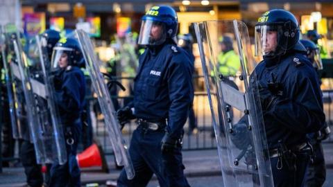 Police officers with riot shields walk along a road in Epsom.