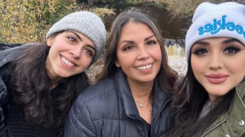 Three woman stand together smiling at the camera 