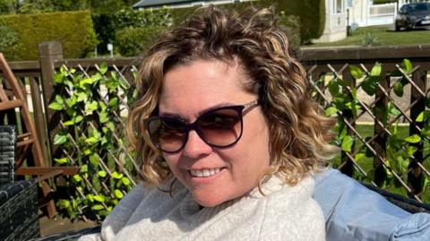 A close-up image of a woman wearing sunglasses. She is smiling and looking into the camera.
