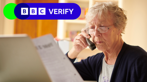 A stock image of a grey-haired woman looking at a bill and her laptop while she is on the phone