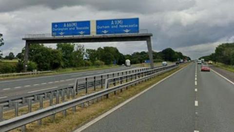 A street image of the northbound and southbound carriageways. Two blue sign tower over the northbound carriageway which read "A66 (M) Darlington and Teesside" and "A1(M) Durham and Newcastle".