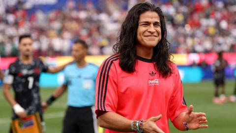 Cristo Fernandez smiling and clapping his hands while wearing a red Adidas t-shirt
