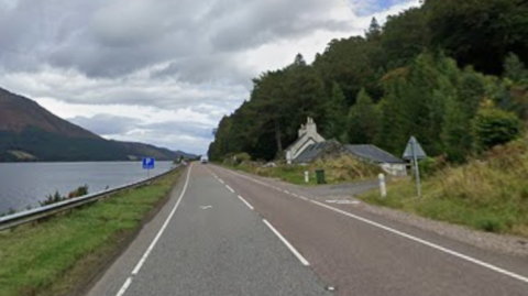 A straight stretch of the A82 by the side of Loch Lochy. There is a low, white-walled house.