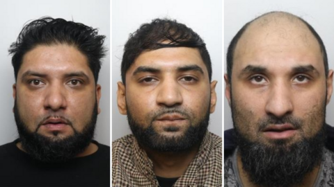 A composite of three mugshots placed side by side. Amar Ilyas on the left is shown from the shoulders upward, facing directly toward the camera. He has dark hair styled upward and slightly back, along with a full beard and moustache. He is wearing a dark top, and the face is evenly lit, with no strong shadows. 
In the centre portrait, Kamran Ilyas is presented in a similar head-and-shoulders format, also facing forward. He has short, dark hair and a full beard and moustache. The clothing appears to be a brown or patterned garment or shirt.
In the right portrait, Kamar Ilyas is shown with very little or no hair on the head and a full beard. He is wearing a dark or muted jacket or top.