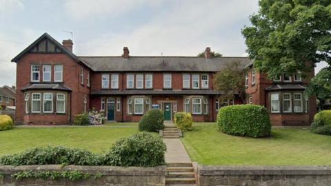 Primrose Lodge. The building is a large red brick detached property. It has a large green lawn and has two floors.