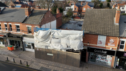 A drone image showing a row of properties - the aerial shot shows that two buildings in the middle of the terraced street have been demolished. Scaffolding covers the front of where the buildings were.
