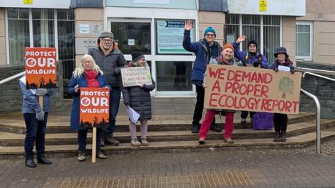 Campaigners outside Cumberland Council headquarters. They hold reading, protect our wildlife. Another reads, we demand a proper ecology report.
