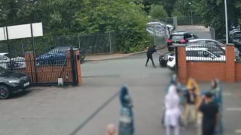 A man in a black shirt puts his hand on the bonnet of a car moments before he is knocked over