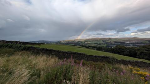 A rainbow and thunder clouds with some sunshine in the distance over the hills of north-west England