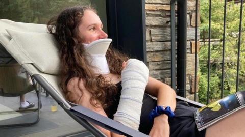 Pfeiffer Georgi sat in a chair wearing a neck brace, with her arm in a cast