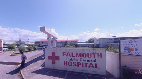 Sign saying Falmouth Public General Hospital with hospital in the background