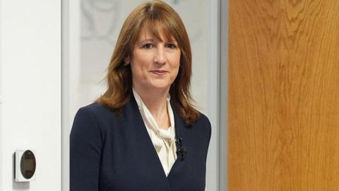 Rachel Reeves steps through a doorway wearing a blue suit and white shirt as she visits an OpenReach training centre in Crawley, West Sussex