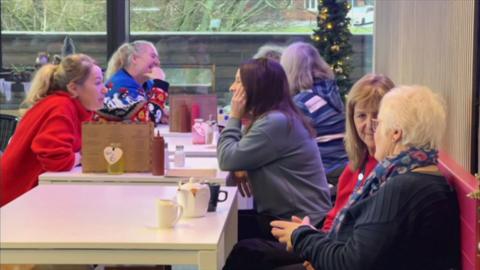 A photo of seven women sat at three tables drinking coffee
