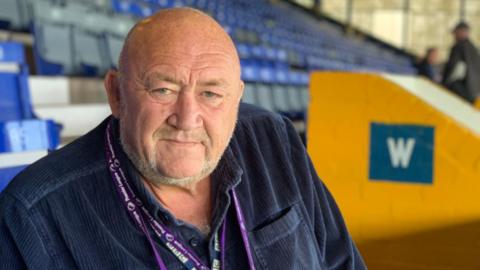 John 'Willo' Williams sitting in the stands of an empty football stadium.