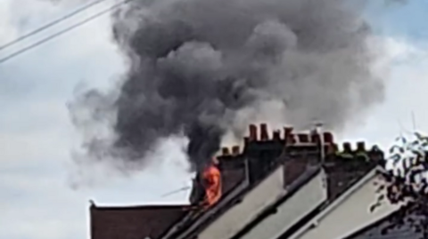 Flames and smoke billow from the roof a terraced house.