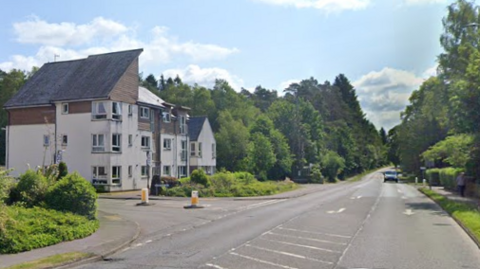 A wide road with white houses on the left