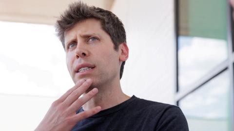 OpenAI chief Sam Altman on an outdoor patio looking pensive and touching his hand to his chin.