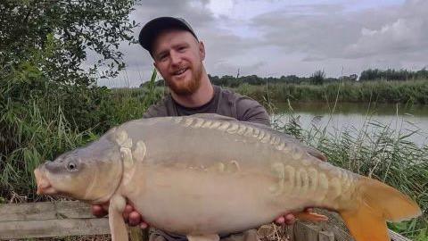 Luke Organ in front of a body of water, holding a large fish