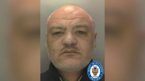 Mugshot of Conrad Byrd. He is bald and has a grey stubble beard and is looking at the camera 