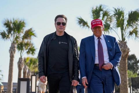 Elon Musk and Trump walk side by side. Musk is wearing black sunglasses and Trump is wearing a Make America Great Again cap