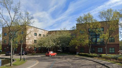 A Google Streetview screenshot of Doxford International Business Park in Sunderland. A road leads to a large office block with parking spaces at the front.