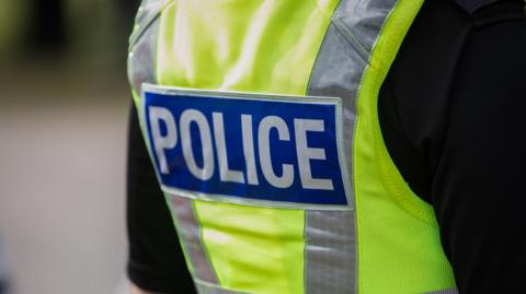 A generic picture of the back of a police officer, who is wearing a florescent vest and a black long-sleeved top 