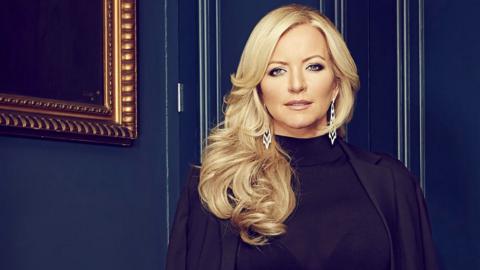 photo of Baroness Michelle Mone stood in front of dark blue wall with black outfit