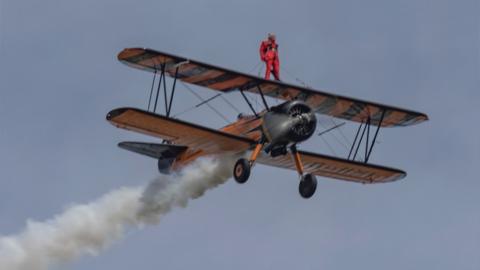 Woman standing on aeroplane. There is steam coming out of the back and it's in the sky.