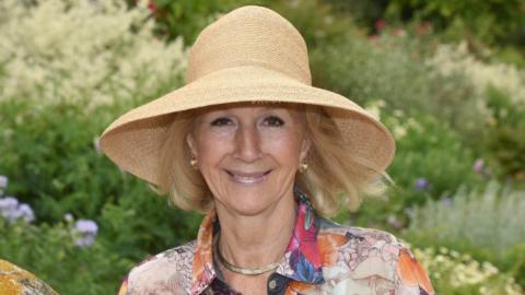 Bunny Campione, who is standing in a garden while wearing a large hat and floral shirt. She is smiling at the camera.