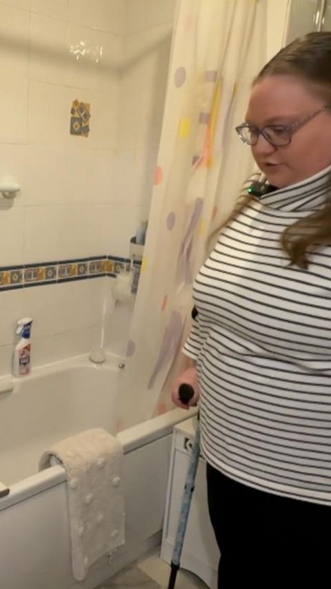 A woman in a black and white striped top stands next to a bath.