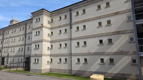 Peterhead Prison with dozens of small windows and barbed wire round the top of an austere four-storey building