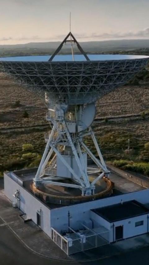 A large antenna on top of a building. It is pointed up towards the sky. The sky is grey and cloudy.