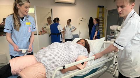 A student led on a hospital bed as two medical students tend to her