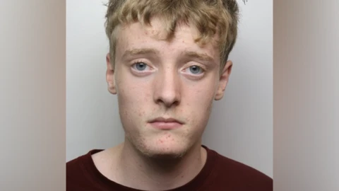 A police mugshot of Jagger Strang. He has fair hair and is wearing a dark red t-shirt