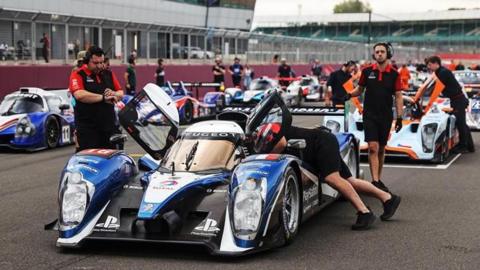 Racing cars on the grid at Silverstone ahead of a race, with mechanics surrounding vehicles.