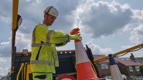 A road construction and maintenance worker actively moving traffic cones on top of his work van.