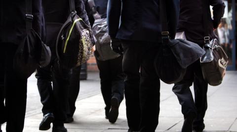 Picture shows children walking to school wearing a black uniform.