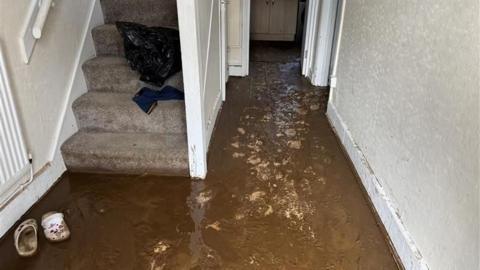 A flooded house with dirty water visible on the downstairs hallway.