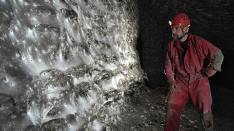 Spiders web on the wall of the cave with a man in red overalls and a red helmet looking at it