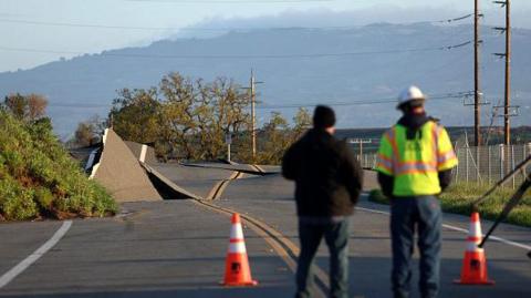 A Pacific Gas and Electric worker looks at a road that buckled when it was undermined by a mudslide during a Bomb Cyclone storm in the week on March 23, 2023 in Novato, California