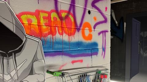 There is a wall that has graffiti on it with the word "read" in orange, red and yellow which is underlined with a blue and purple line. There is also a cardboard cut out of someone in a hoodie with the hood up. There is also a shopping trolley that has been cut in half and stuck to the wall containing spray paint bottles. 