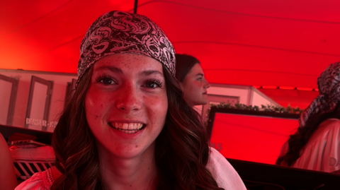 A head and shoulders image of a young woman smiling while wearing a bandana. 