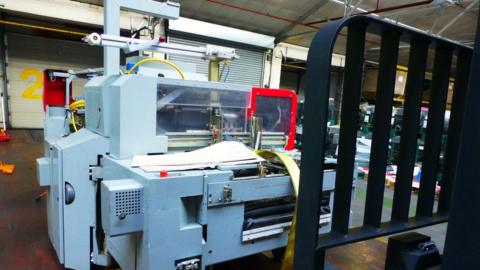 A large grey and silver machine, sitting on a forklift