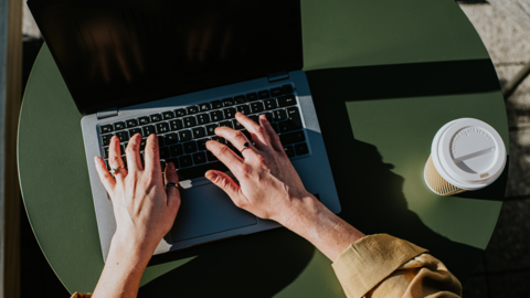 A generic picture of a person using a laptop, they also have a coffee cup.