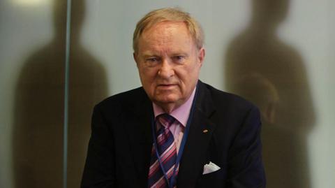 Ludwig Minelli, wearing a suit. 